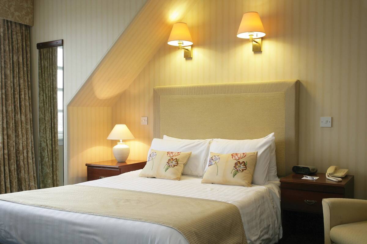 Une chambre d’hôtel avec un grand lit, deux lampes de chevet, une table de chevet avec un téléphone et une chaise.