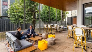 Un espace extérieur aménagé avec un plafond en bois, des canapés gris, des fauteuils en forme de poire jaune et des tables avec des chaises.