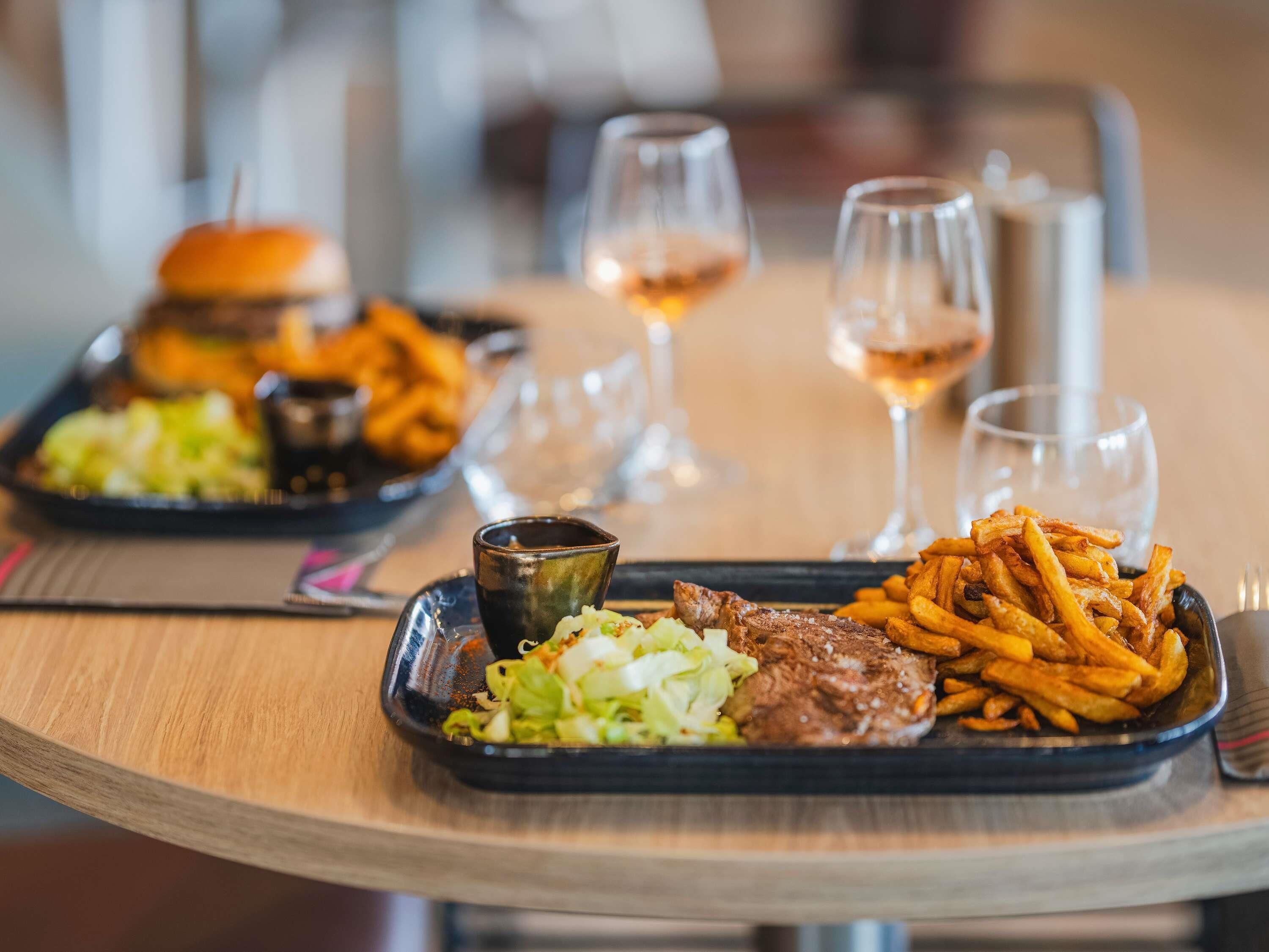 A meal tray with a burger, fries, and salad, accompanied by a glass of wine.