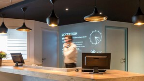 Un comptoir d’accueil doté d’un écran numérique affichant les tarifs des chambres et d’une horloge.
