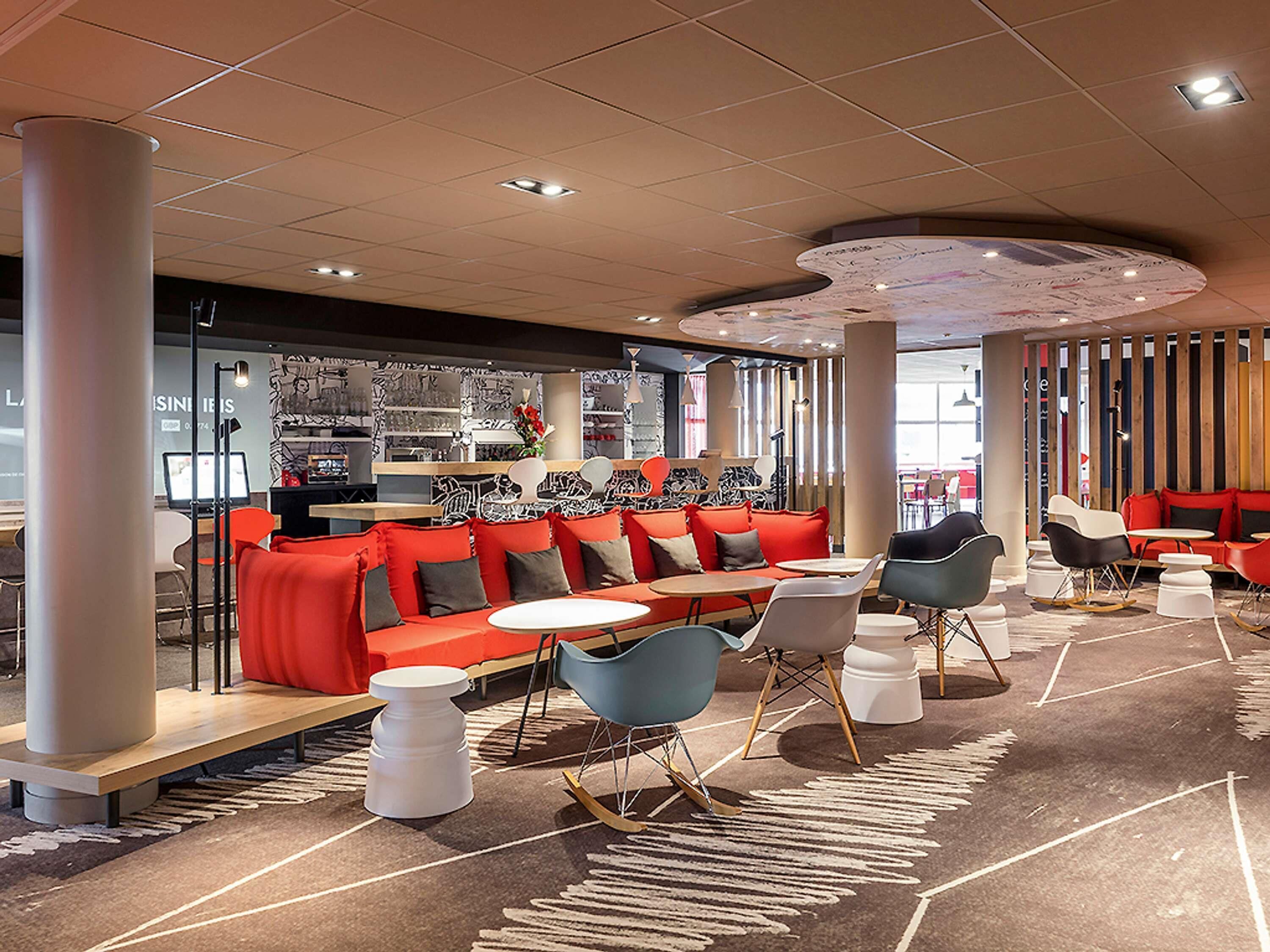 Un restaurant moderne avec des sièges rouges, des tables blanches et un tapis à motifs.