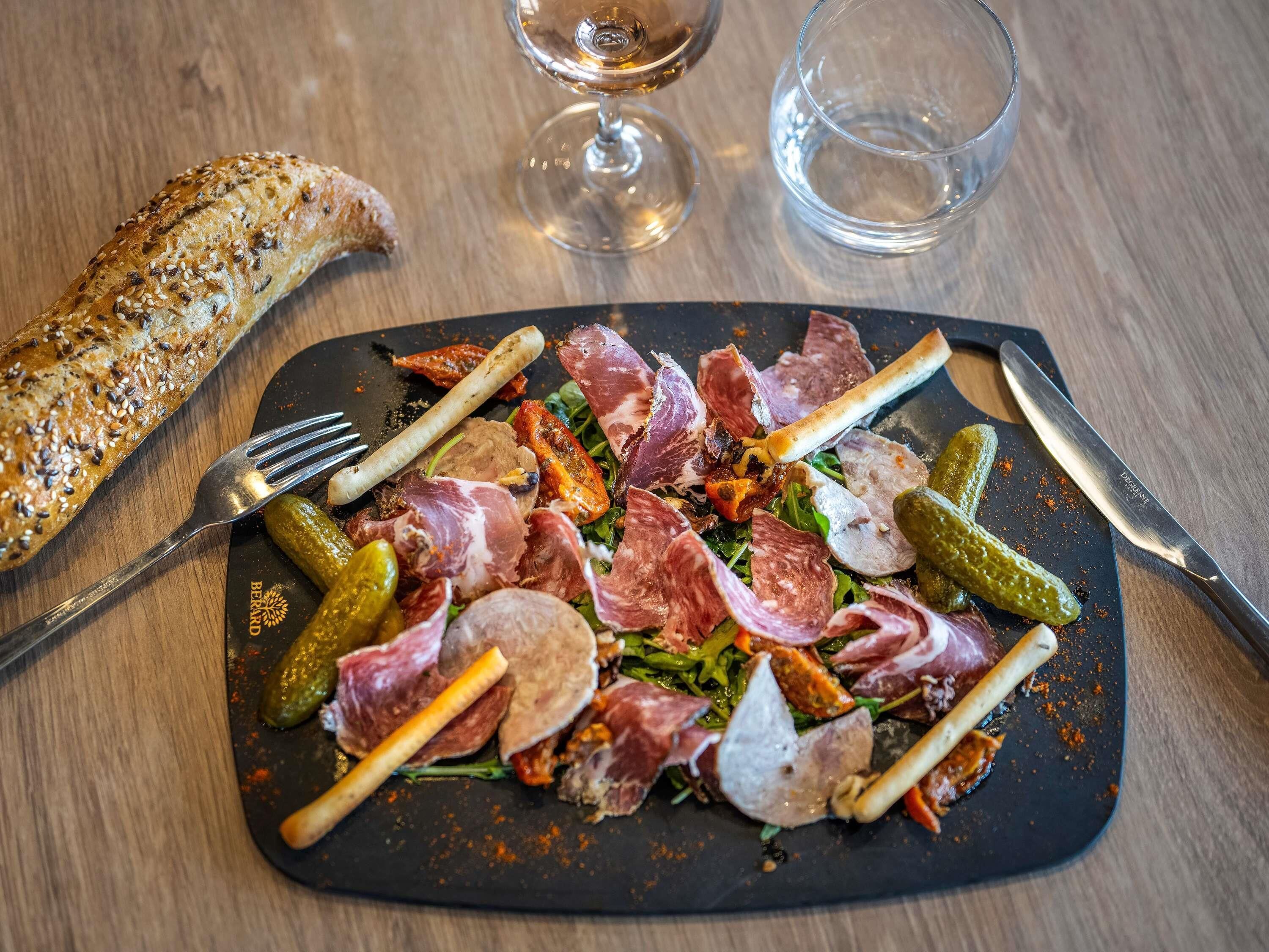 Un repas composé de différentes sortes de viande, de cornichons et d’une miche de pain, le tout servi sur une assiette noire.