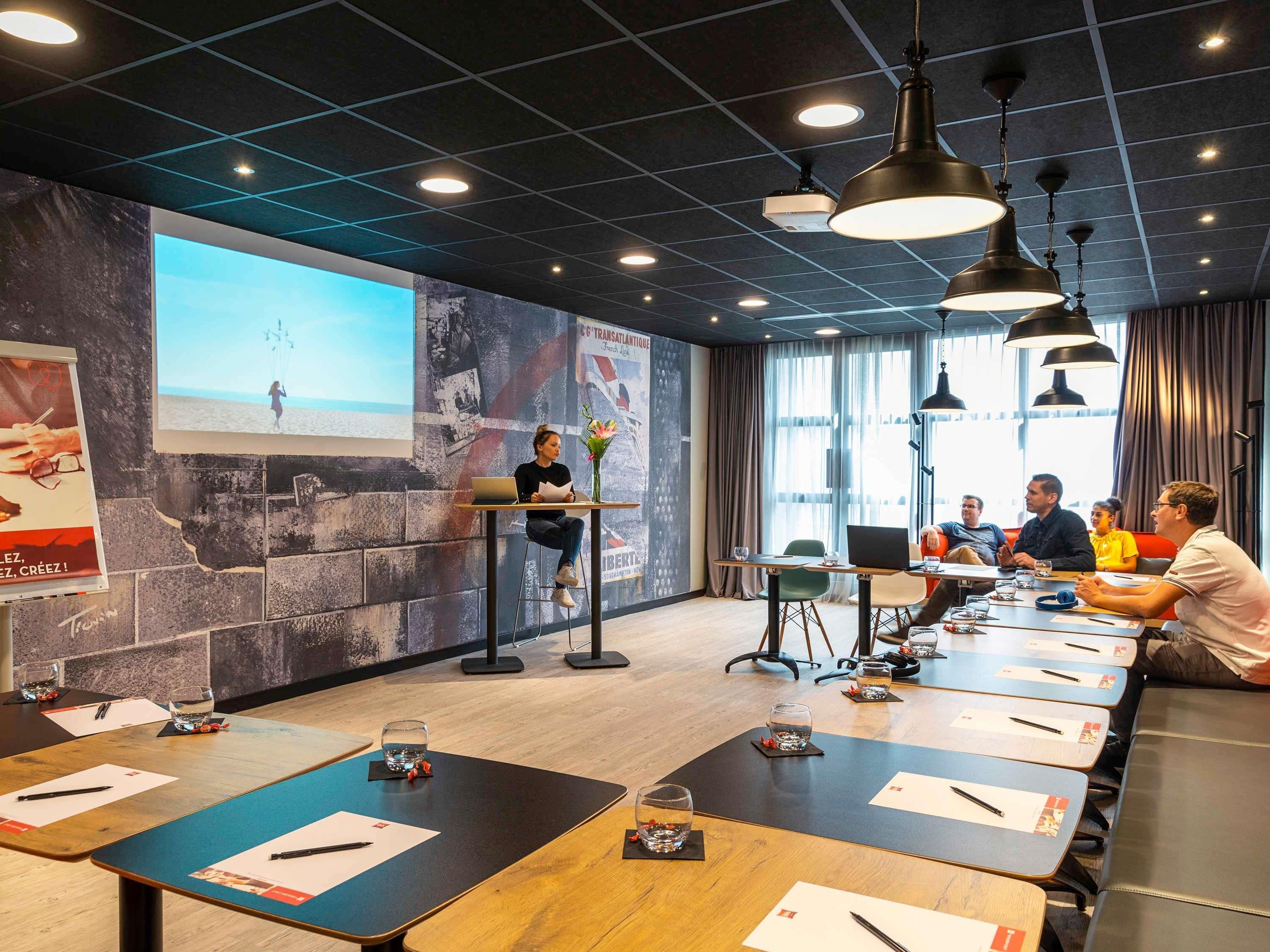 A conference room with a presentation screen, a seated audience, and a speaker.