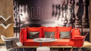 Un espace détente avec un canapé rouge, des chaises blanches et une table ronde.