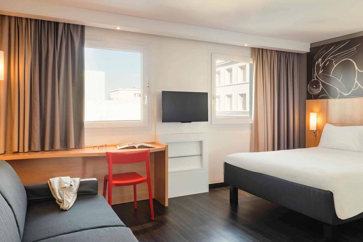 A hotel room with a bed, a desk with a chair, a television, and a couch.