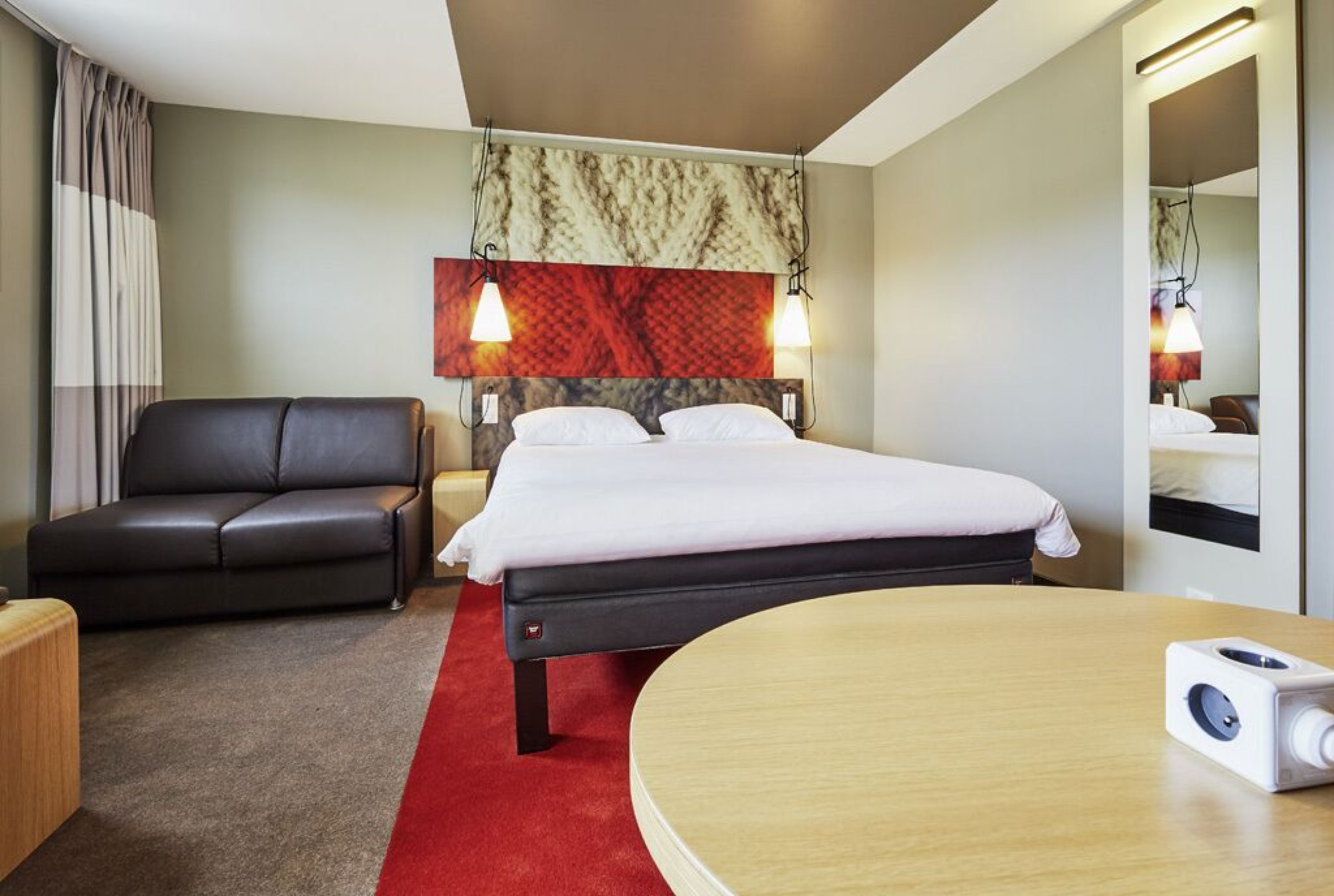 A hotel room with a bed, a leather sofa, a round table, and a red carpet.
