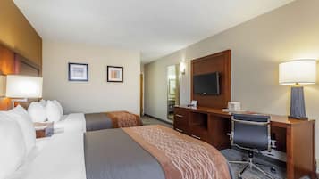 Quarto de hotel com uma cama, uma escrivaninha, uma cadeira, uma TV e duas molduras na parede.