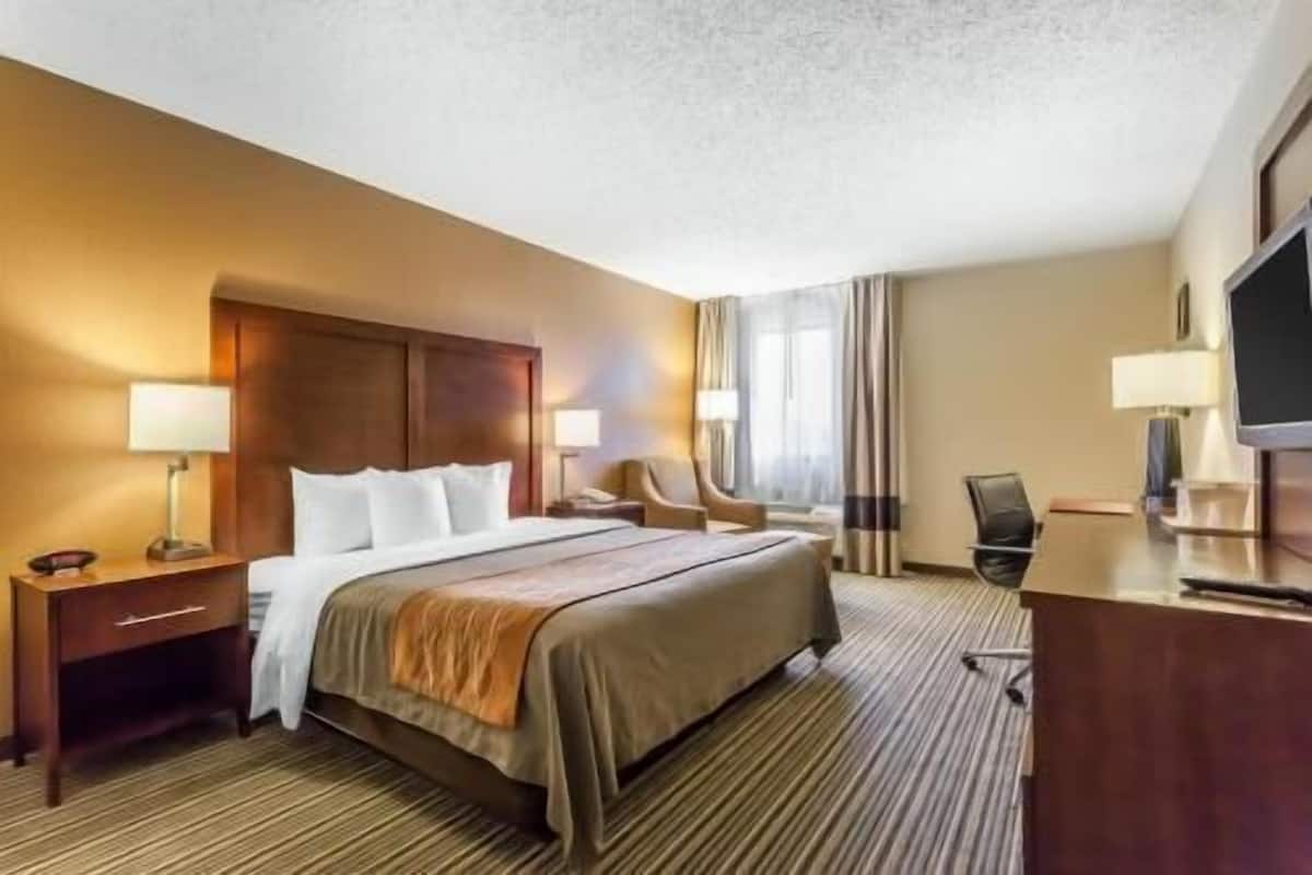 A hotel room with a large bed, a desk, a chair, and a television.
