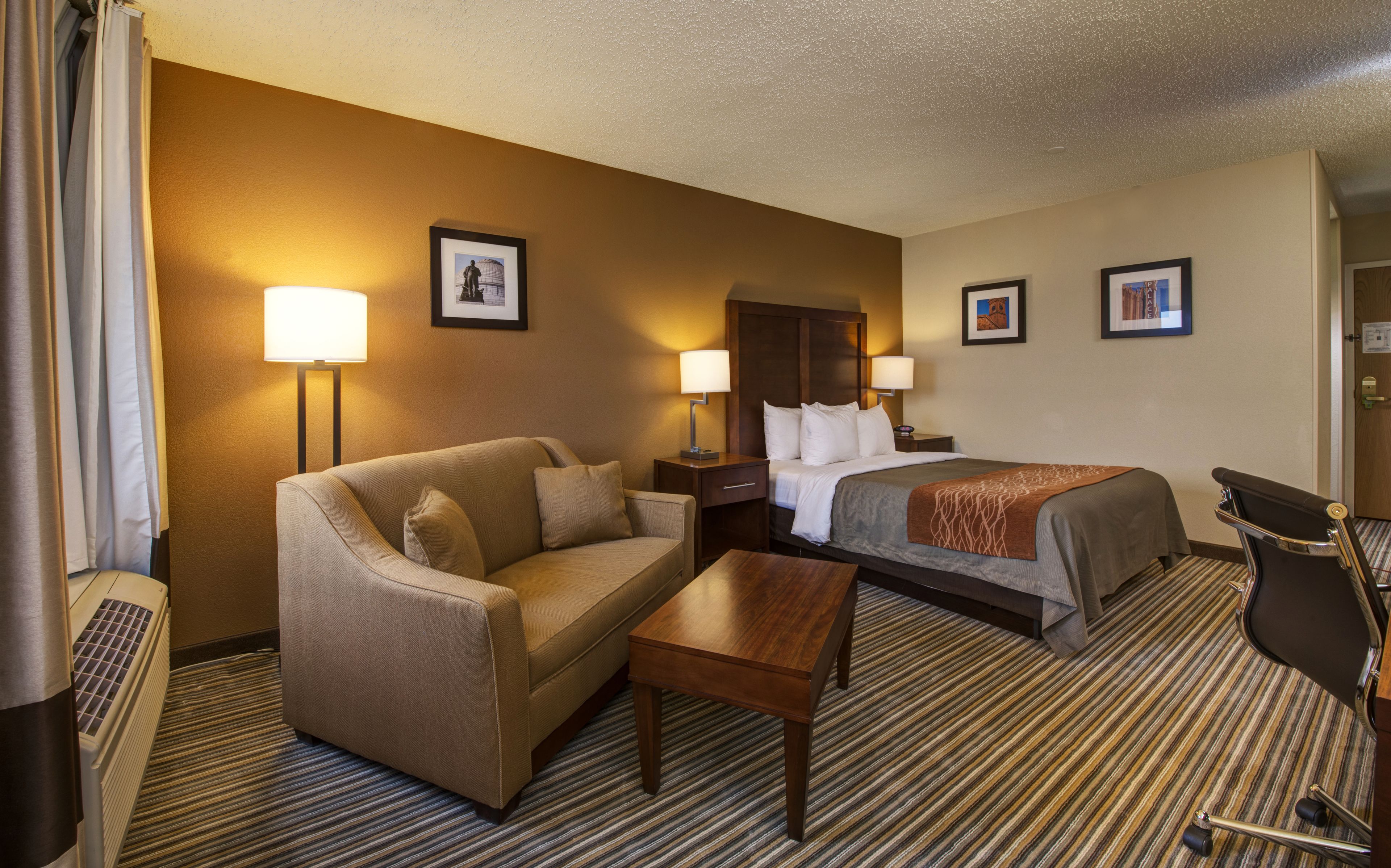 A hotel room with a bed, a sofa, a desk, and two bedside lamps.