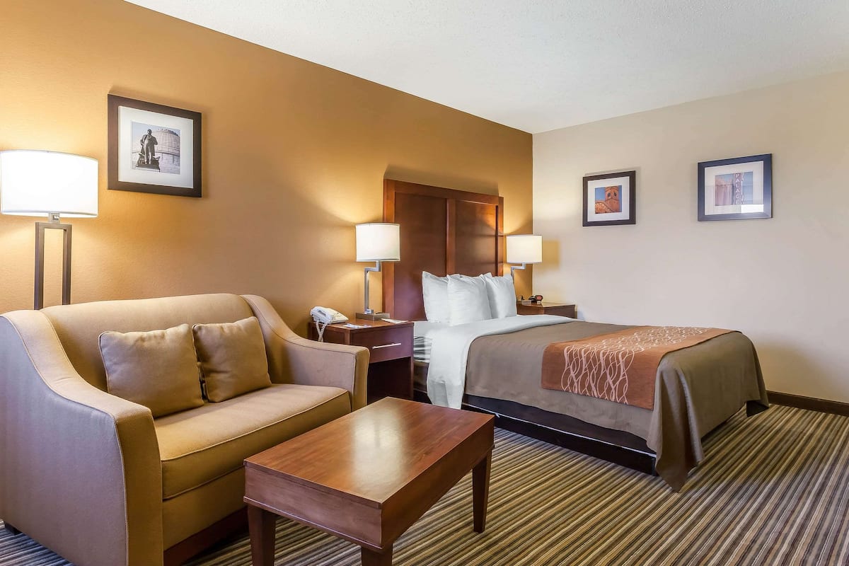 A hotel room with a sofa, a bed, a nightstand, and two wall-mounted lamps.