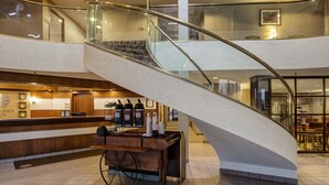 A modern hotel lobby with a curved glass staircase, a reception desk, and a cart with bottles. - Comfort Inn Hall of Fame (Canton)