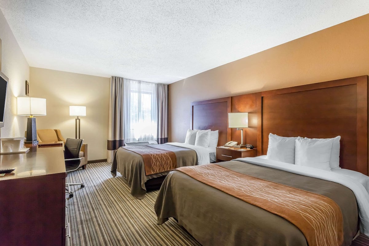 A hotel room with two beds, a desk with a lamp, a chair, and a TV.