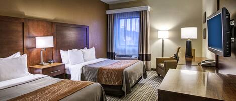 A hotel room with two beds, a desk with a telephone, a television, and a window with curtains.