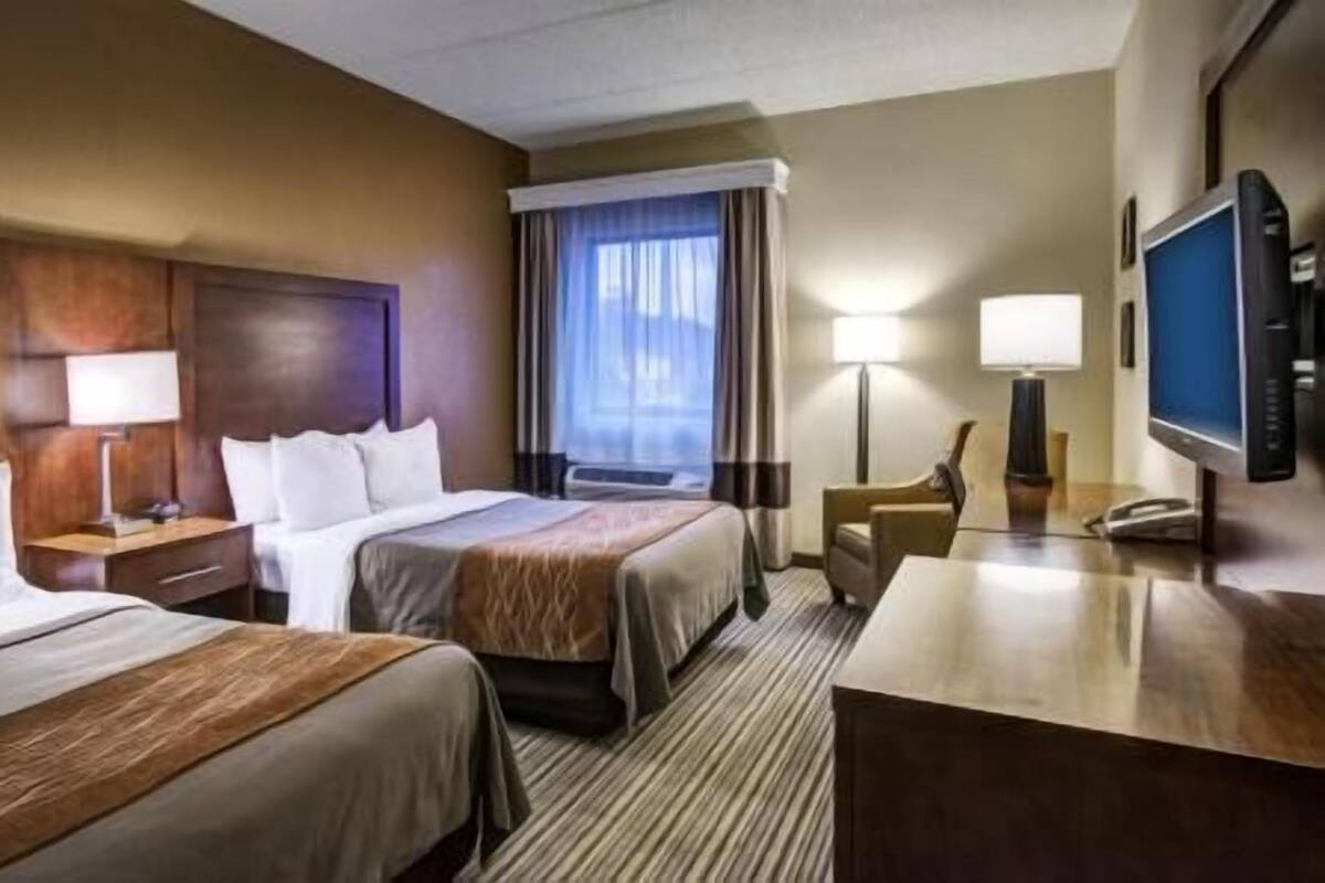A hotel room with two beds, a desk, a TV, and a window with curtains.