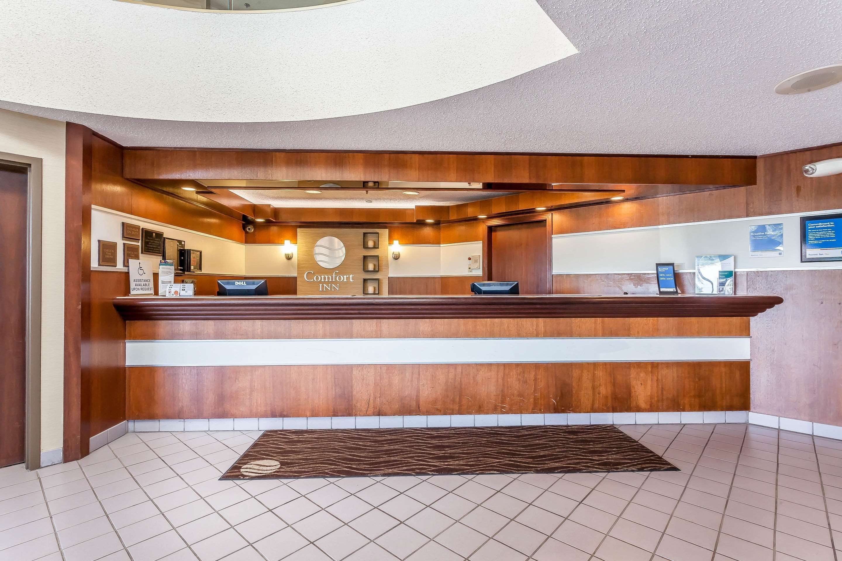 A hotel reception desk with a wooden finish, a sign reading "Comfort Inn," and a tiled floor.
