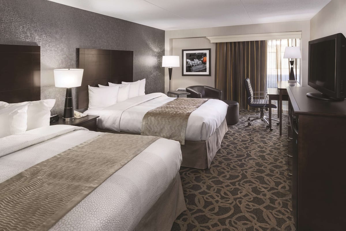 A hotel room with two beds, a desk, a chair, a television, and a framed picture on the wall.