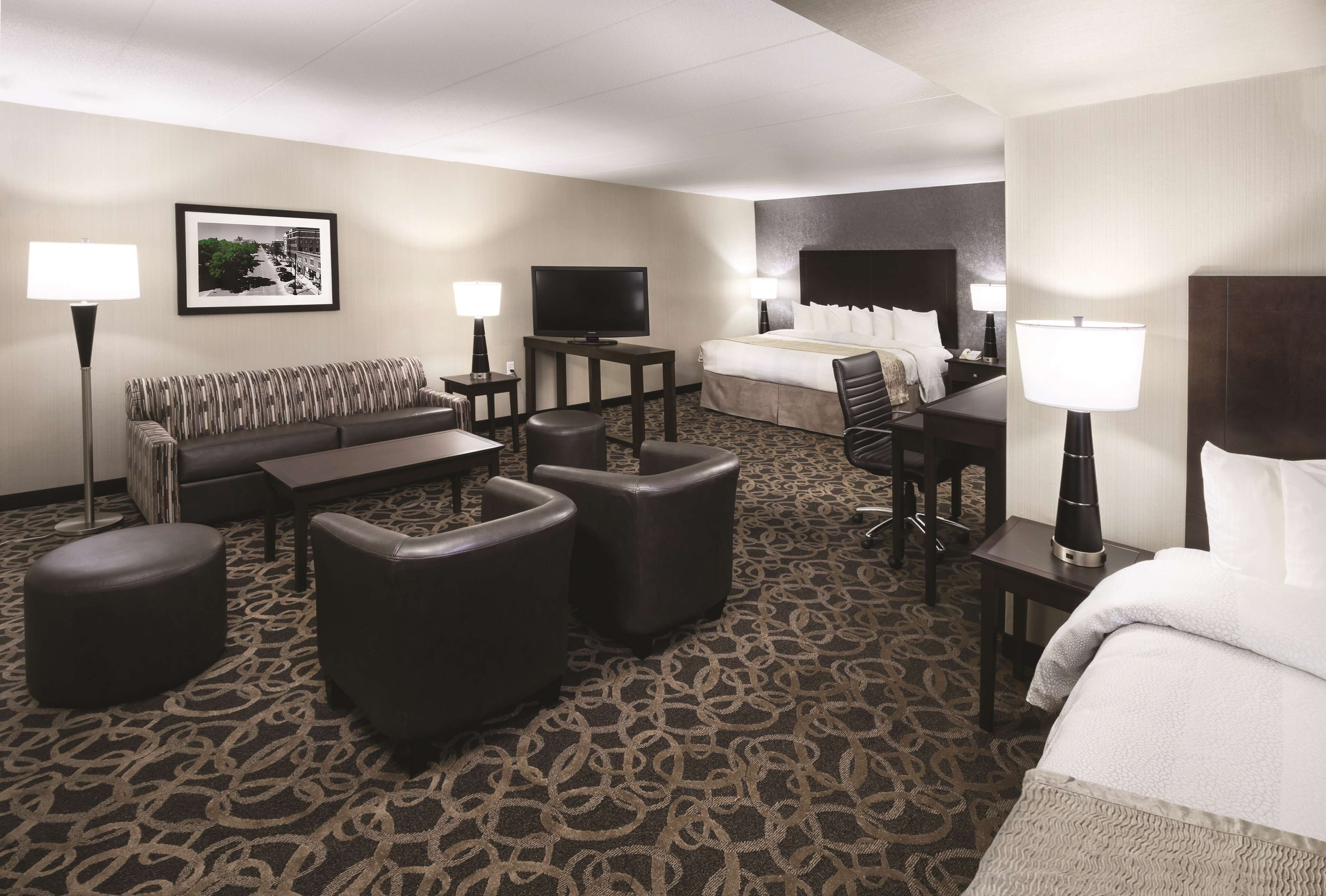 A hotel room with a bed, a sofa, a desk, a TV, and two lamps.
