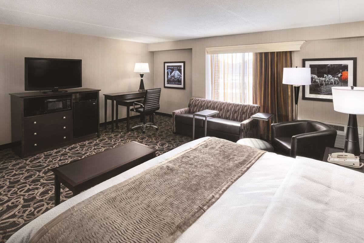A hotel room with a large bed, a desk with a chair, a television, a sofa, and a small table.