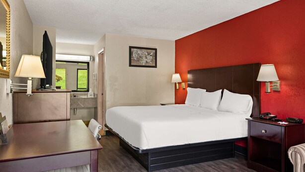 Una habitación de hotel con cama, mesitas de noche, un escritorio y un espejo.