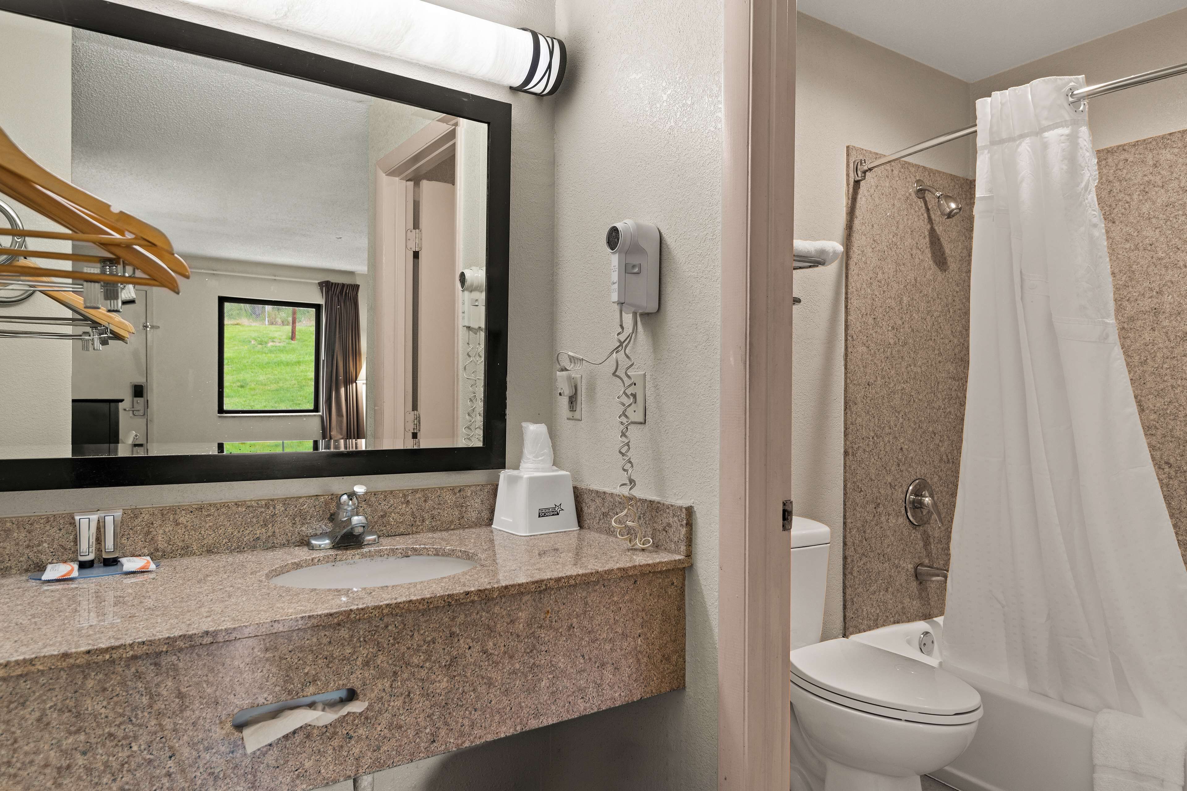 A bathroom with a granite countertop, a mirror, a hair dryer, a shower curtain, and a toilet.