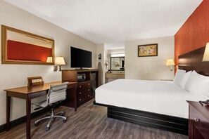 A hotel room with a bed, desk, chair, TV, and a mirror.