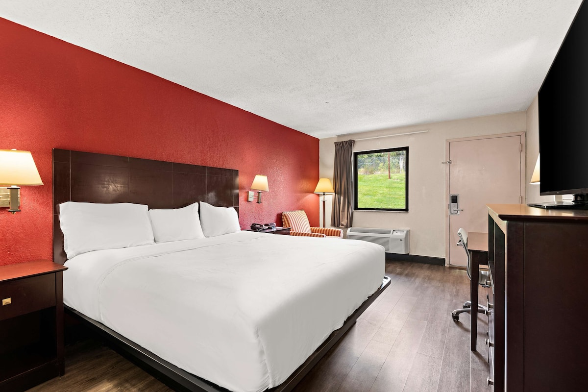 Une chambre d’hôtel avec un grand lit, deux lampes de chevet, un bureau avec une chaise, une télévision et une fenêtre donnant sur l’extérieur.