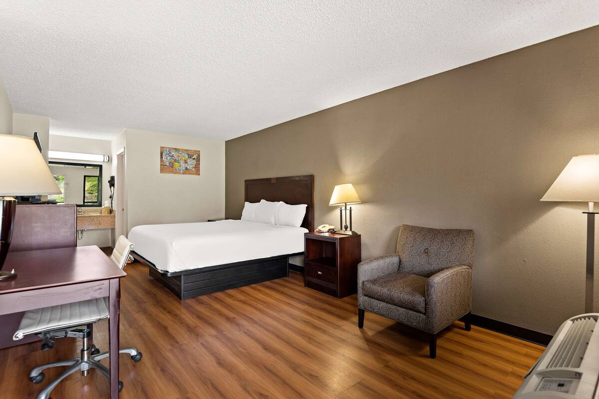 Une chambre d’hôtel avec un lit, un bureau, une chaise et deux lampes.