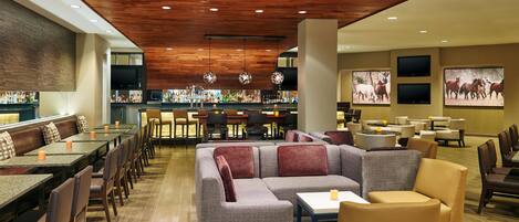 A spacious lounge area with a bar in the background, comfortable seating, and a wooden ceiling.