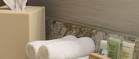 A bathroom vanity with a tissue box, a rolled towel, and a tray with toiletries.