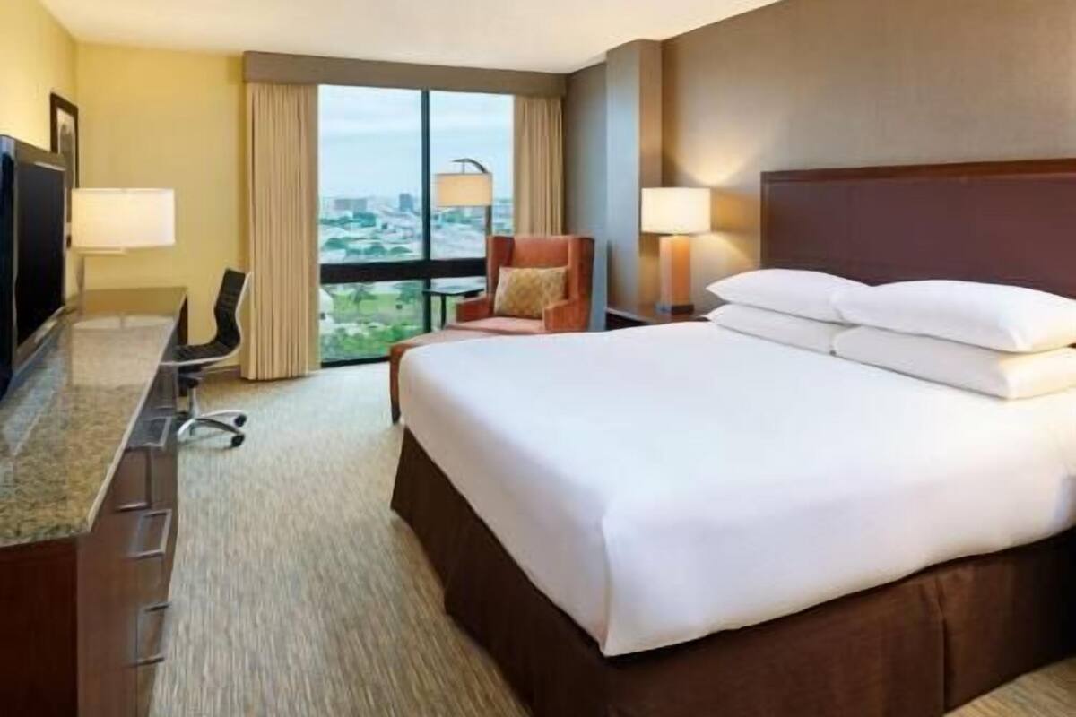 Ein Hotelzimmer mit Bett, Schreibtisch, Stuhl und einem großen Fenster.