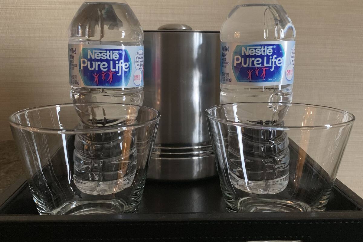 Un plateau contenant deux bouteilles d’eau Nestlé Pure Life et un distributeur d’eau en acier inoxydable, accompagné de quatre verres transparents.