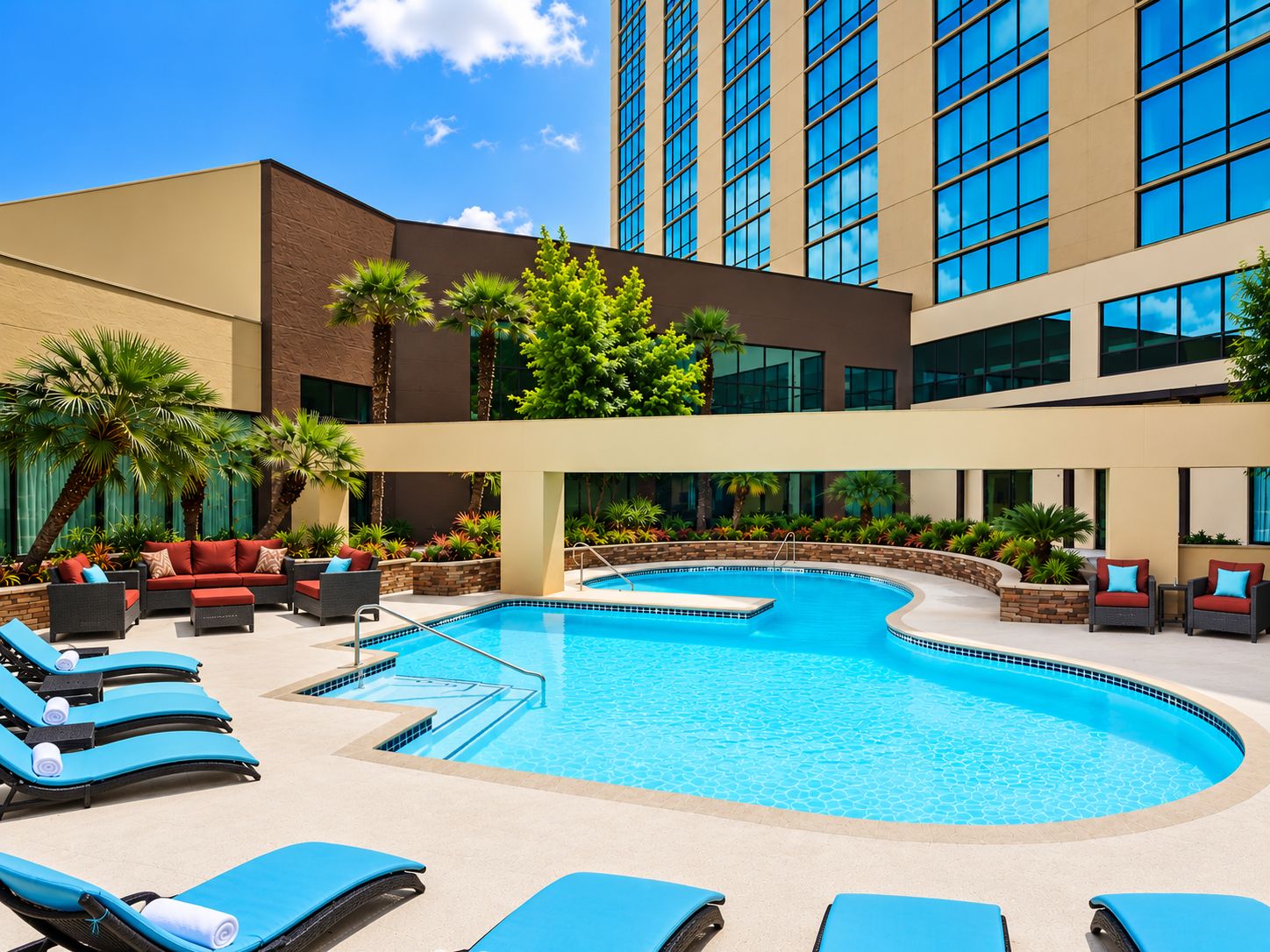 A hotel pool area with lounge chairs, a swimming pool, and a building with large windows.