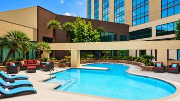 A hotel pool area with lounge chairs, a swimming pool, and a building with large windows.
