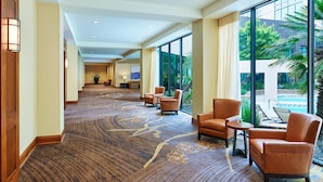 En hotellobby med ett golv täckt av matta, en sittgrupp, stora fönster och utsikt över en pool.