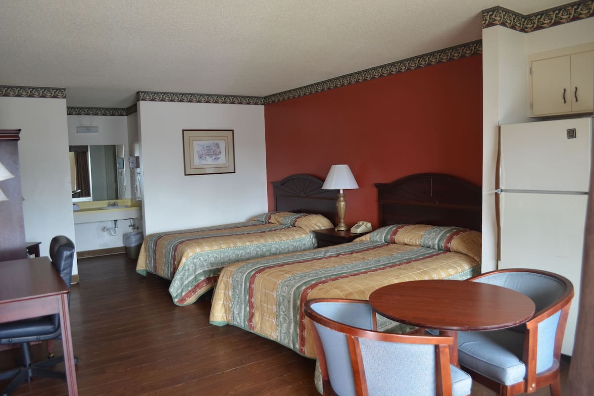 A hotel room with two beds, a desk with a chair, a small table, and a refrigerator.