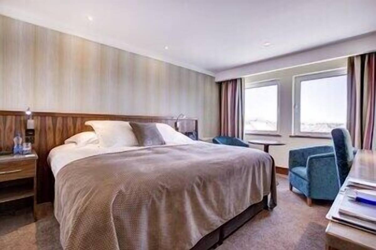 Habitación de hotel con una cama grande, un escritorio con silla, ventana con cortinas y vistas al exterior.