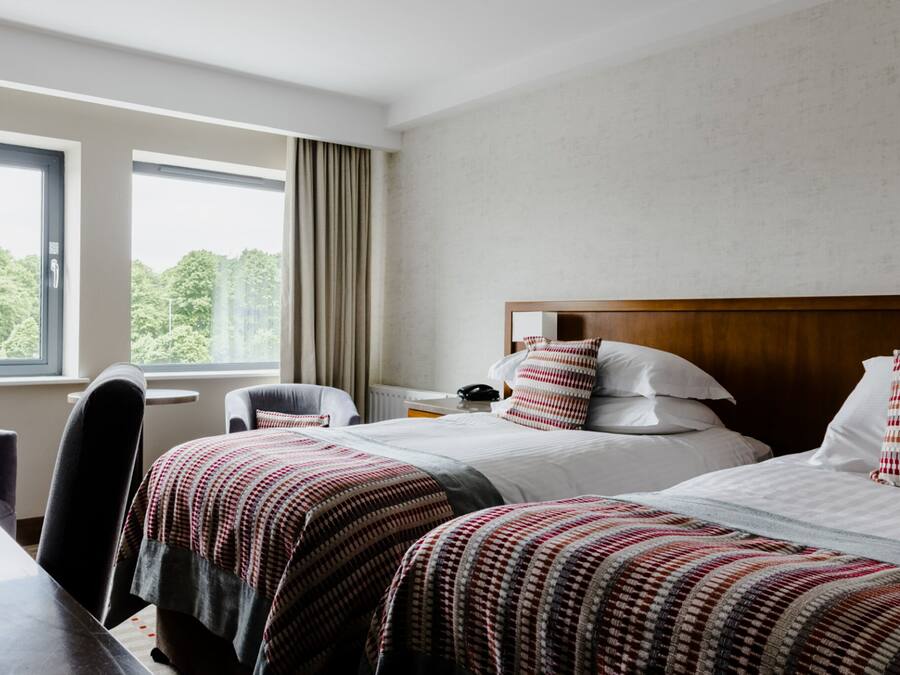 A hotel room with two beds, a desk, and a chair.