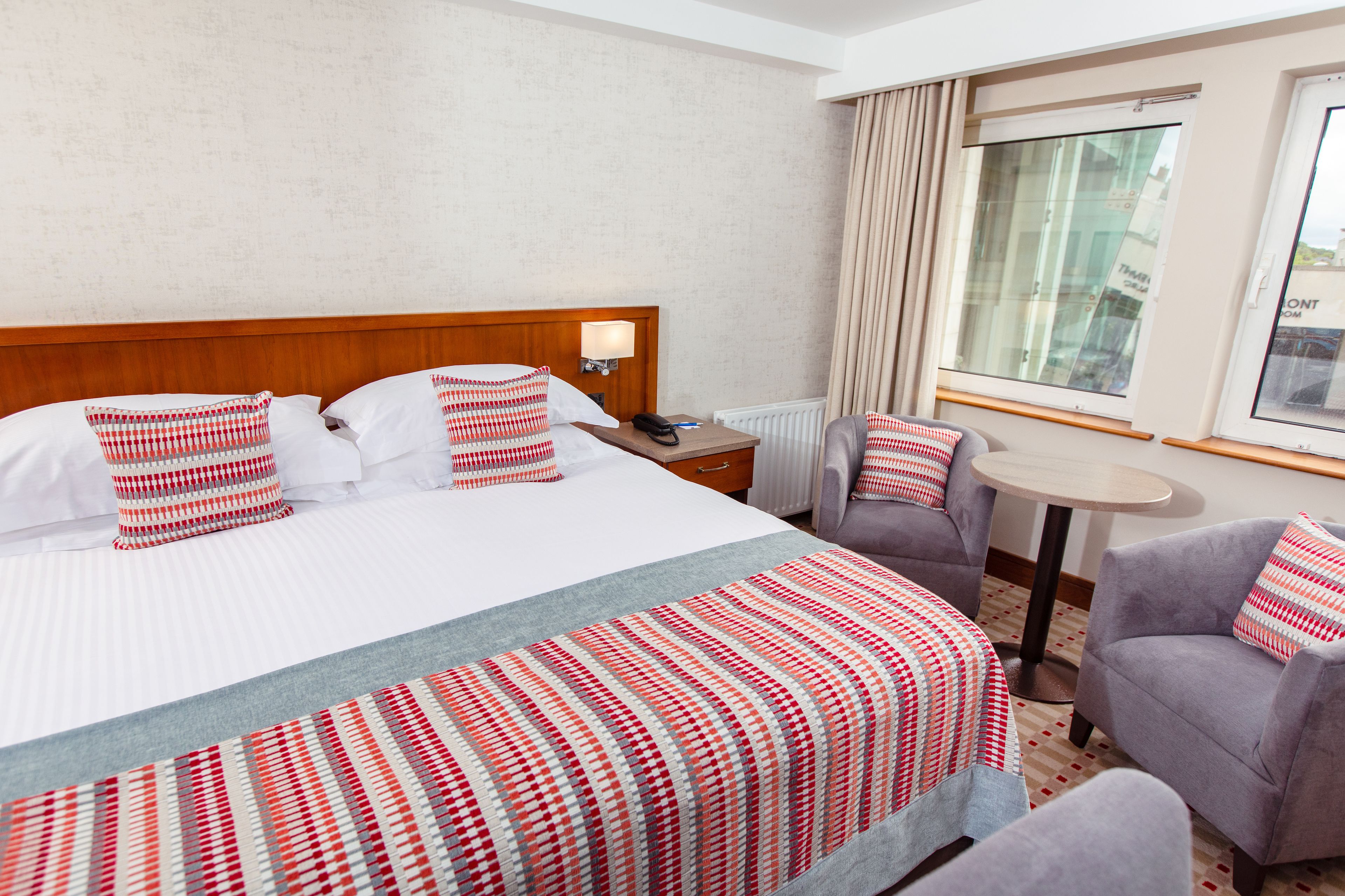 A hotel room with a large bed, two armchairs, a small table, and a window with curtains.