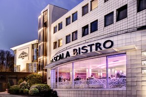 Un bâtiment moderne abritant un restaurant appelé « La Scala Bistro », qui se distingue par ses grandes fenêtres en verre et sa façade bien éclairée.