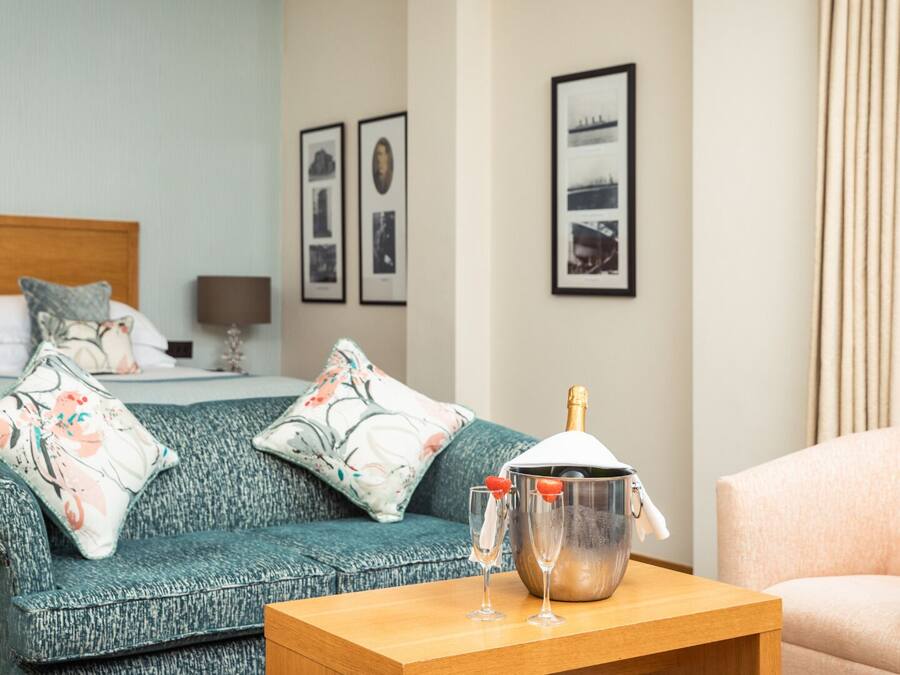 Ein Hotelzimmer mit einem Bett, einer Couch, einem Holztisch mit Champagnergläsern und gerahmten Bildern an der Wand.