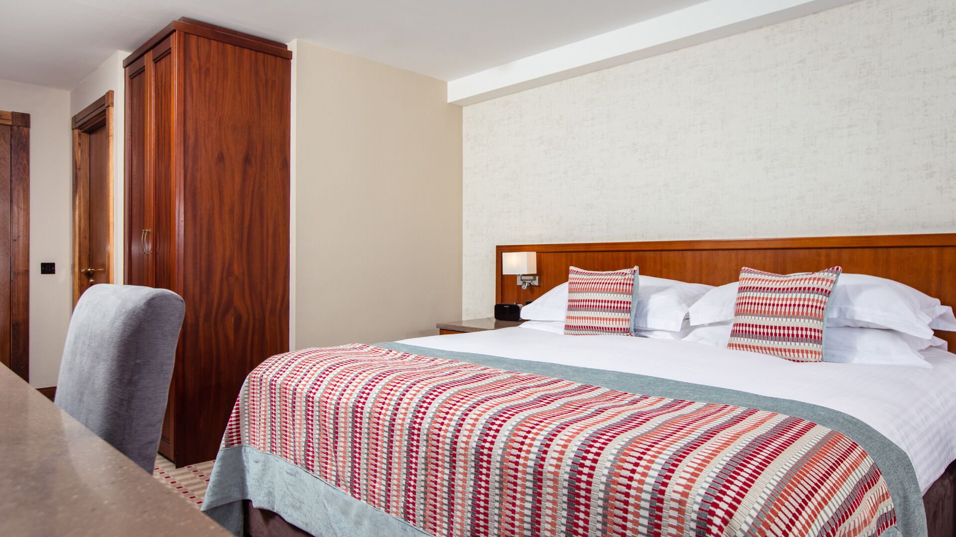 A hotel room with a large bed, a wooden wardrobe, a desk, and a chair.