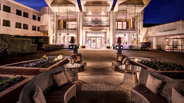 A hotel entrance with a modern design, outdoor seating area, and well-maintained landscaping.