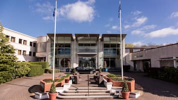 Stunning hotel entrance with a central entrance flanked by flagpoles, surrounded by a beautifully landscaped area with potted plants and outdoor seating.