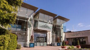 Un hotel moderno con fachada de vidrio, entrada destacada y jardín delantero ajardinado.