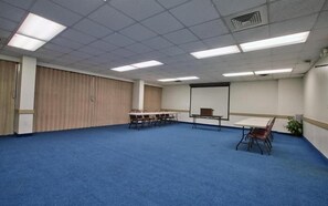 A conference room with a blue carpet, a white table, and a projector screen. - Studio 6 Tallahassee, FL – North Monroe (Tallahassee)