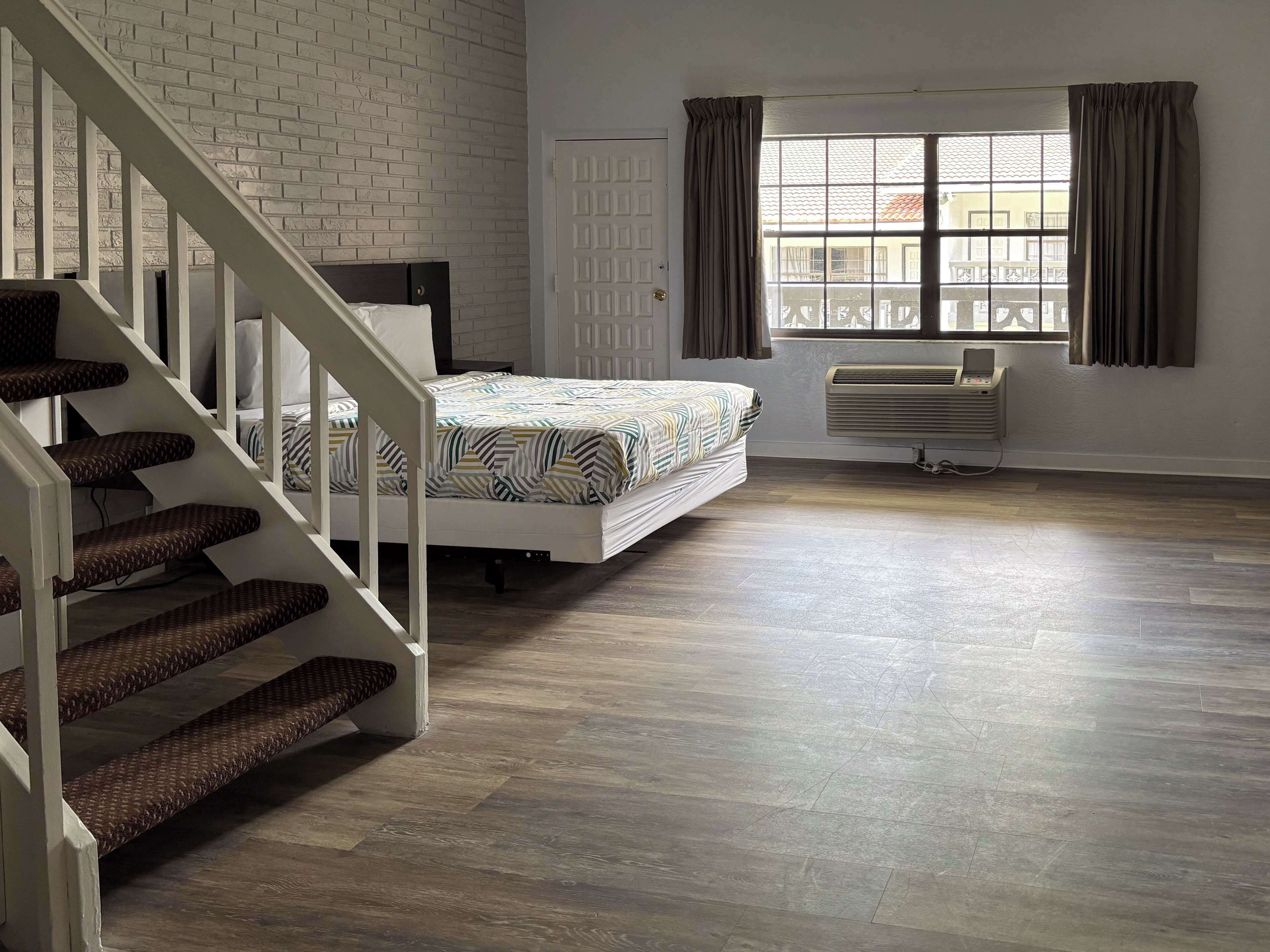 Un dormitorio con cama, una escalera, una ventana con cortinas y un radiador.