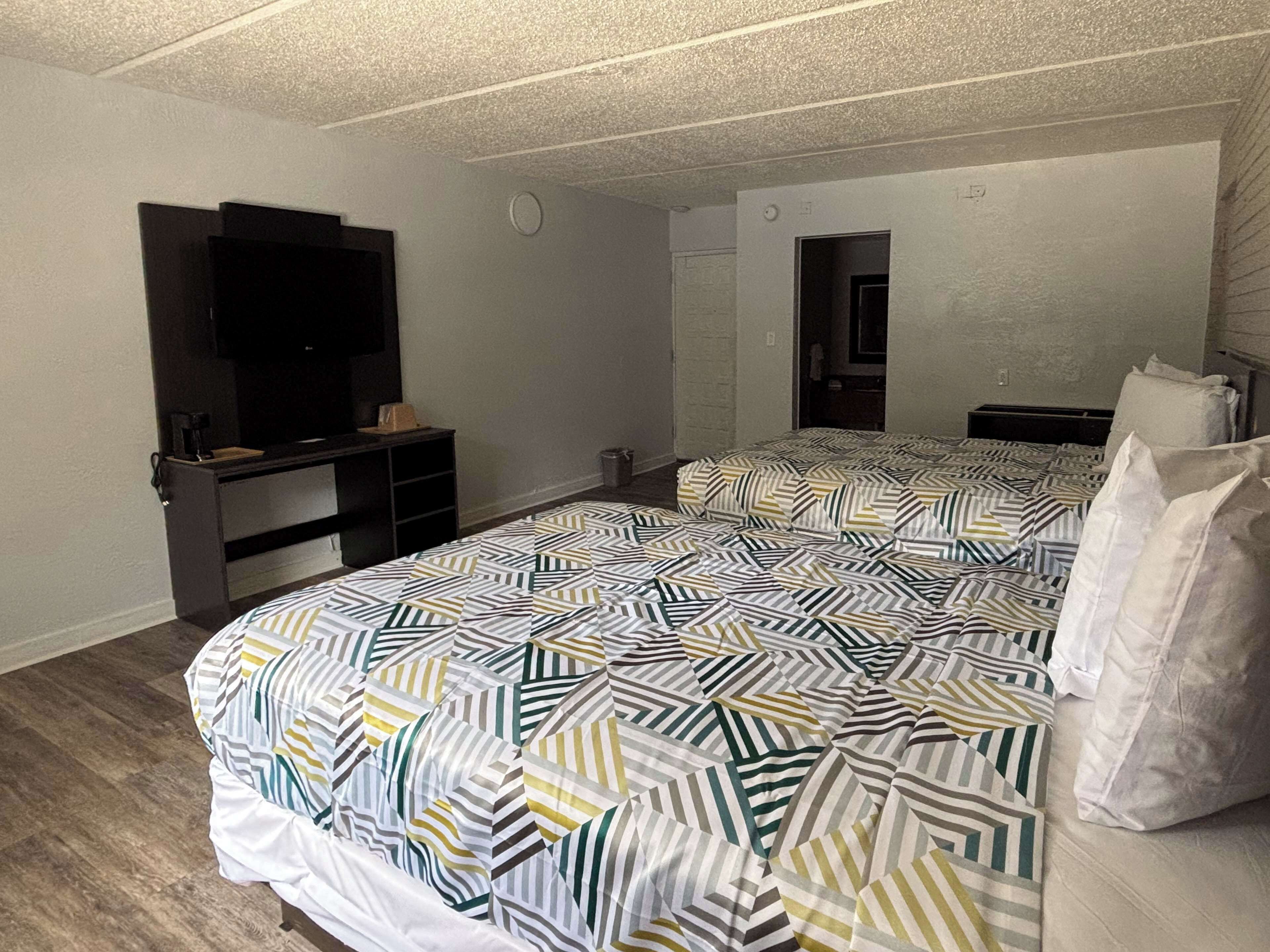 A hotel room with a large bed, a TV on a stand, a desk, and a mirror.