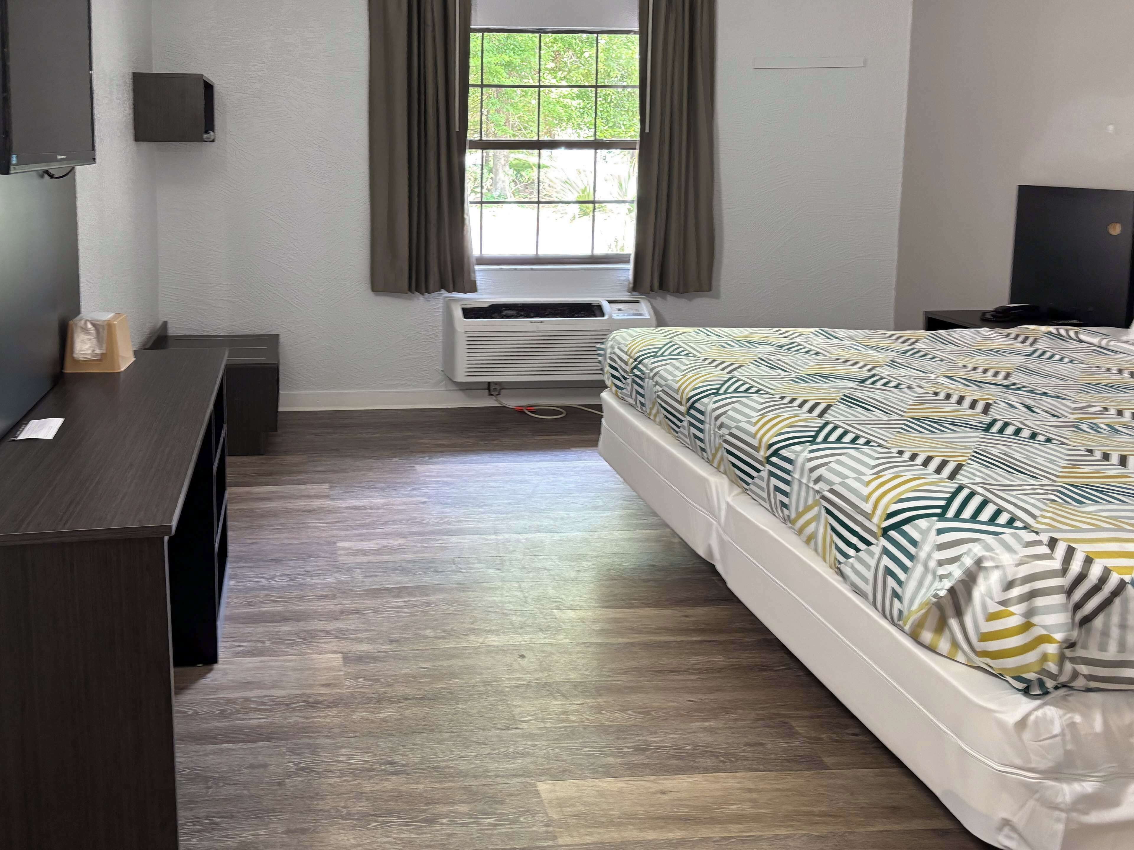 A hotel room with a bed, a desk, an air conditioning unit, and a window with curtains.