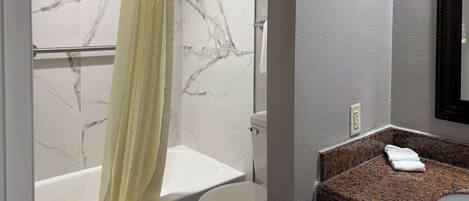 A bathroom with a bathtub, toilet, and granite countertop sink.