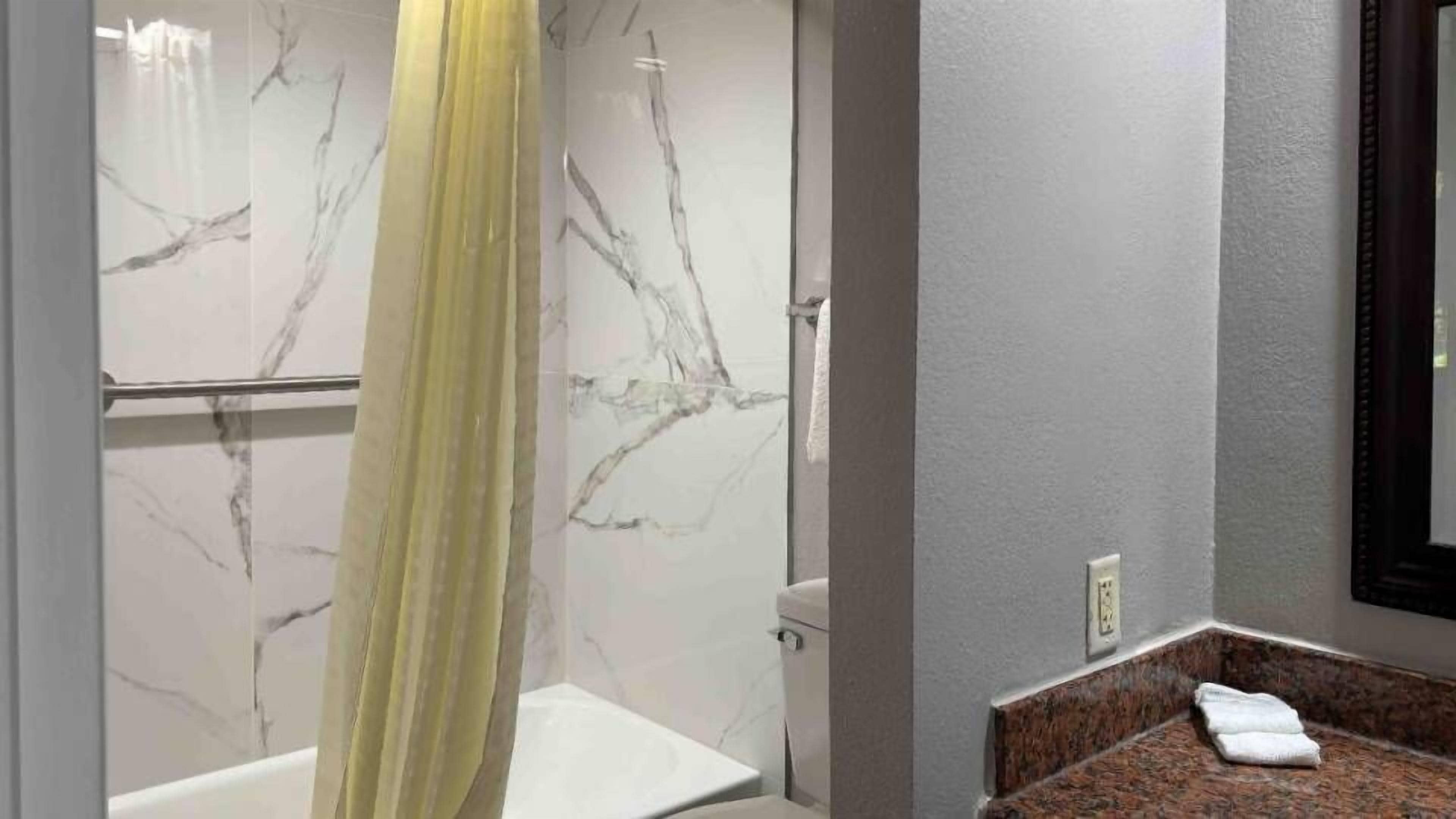 A bathroom with a marble wall, a shower curtain, a toilet, and a sink with a towel.